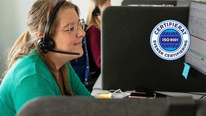 Kvinna som sitter med mikrofon och hörlurar framför datorskärm samt en logotyp för isocertifiering. 