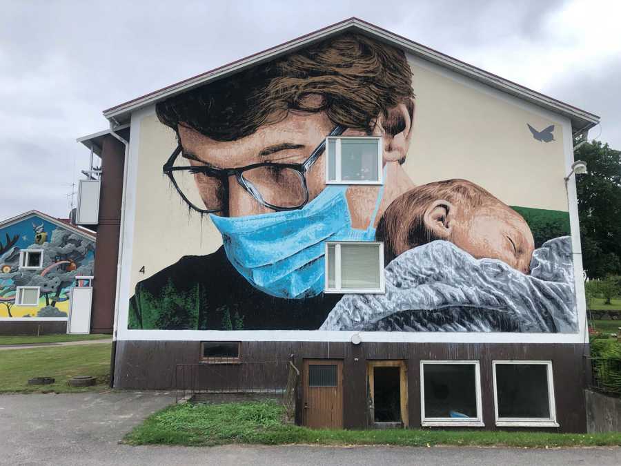 Väggmålning föreställande en man med munskydd som håller en bebis i famnen.