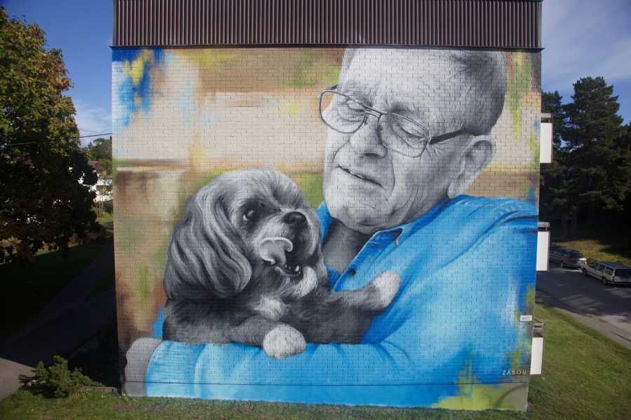 Väggmålning föreställande äldre man med en hund i famnen.