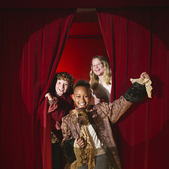 Barn som kikar fram bakom en ridå på en scen.