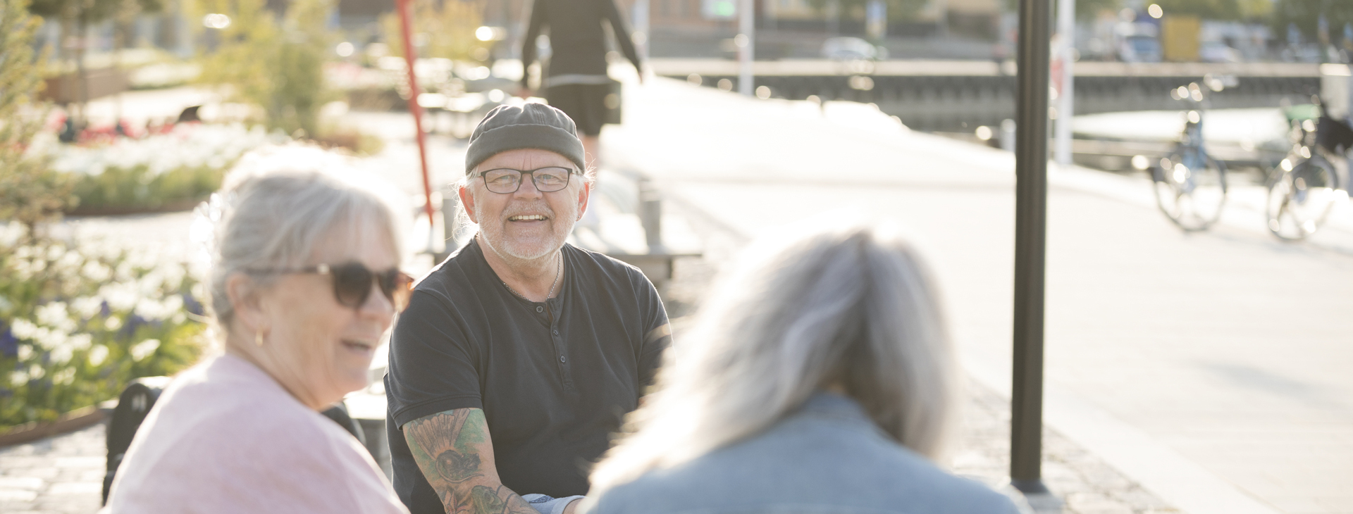 Bild på en glad man och två minst lika glada damer som sitter utomhus och pratar.
