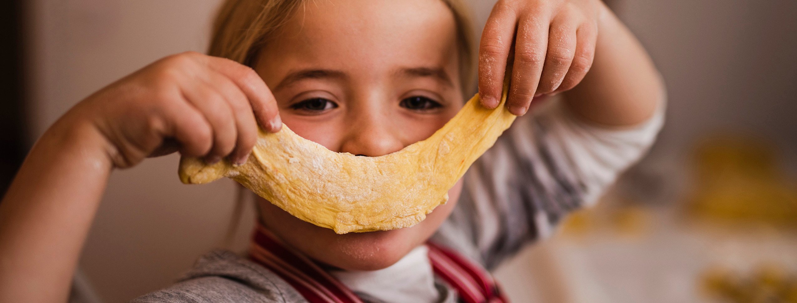 Barn som bakar lussebullar och håller upp en bit deg som en glad mun.