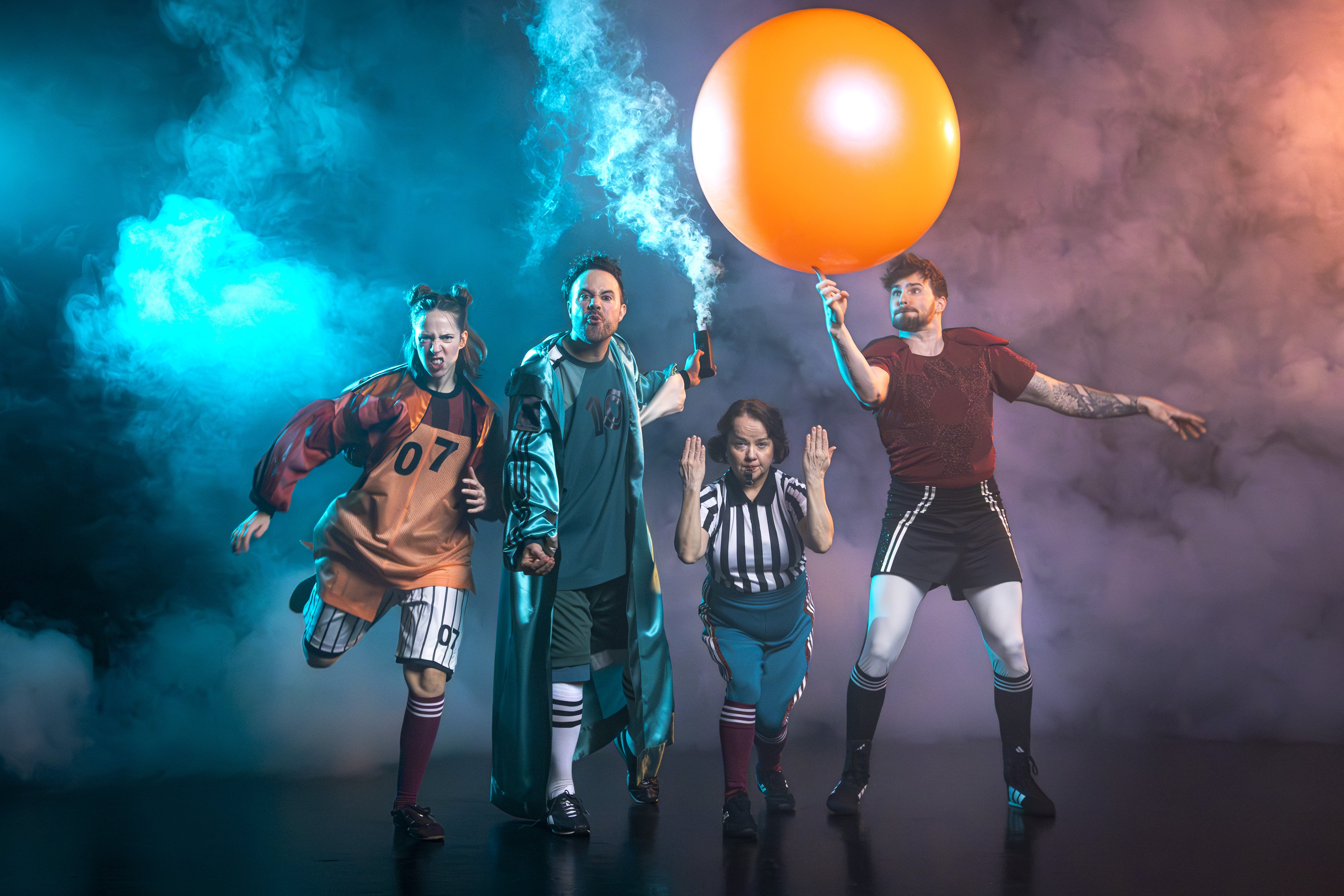 Hela ensemblen står med en stor fotboll och ler mot alla. 