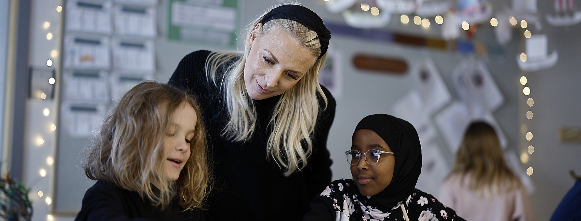 En lärare som interagerar med två av barnen i klassen