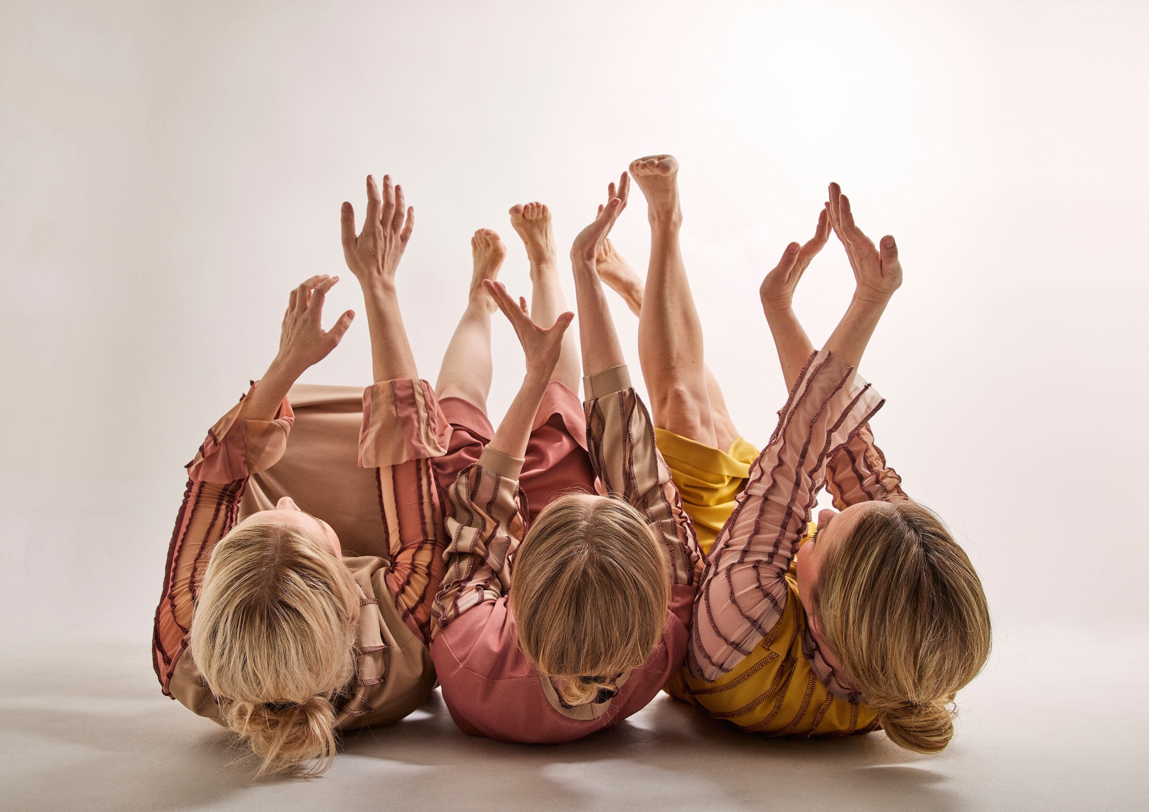 Bildtolkning: Tre dansare ligger på rygg på golvet och sträcker sina armar och ben upp i luften.