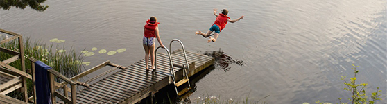 Barn som hoppar från en brygga och badar