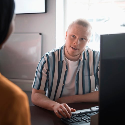 bild på person vid skrivbord som talar med en stående person