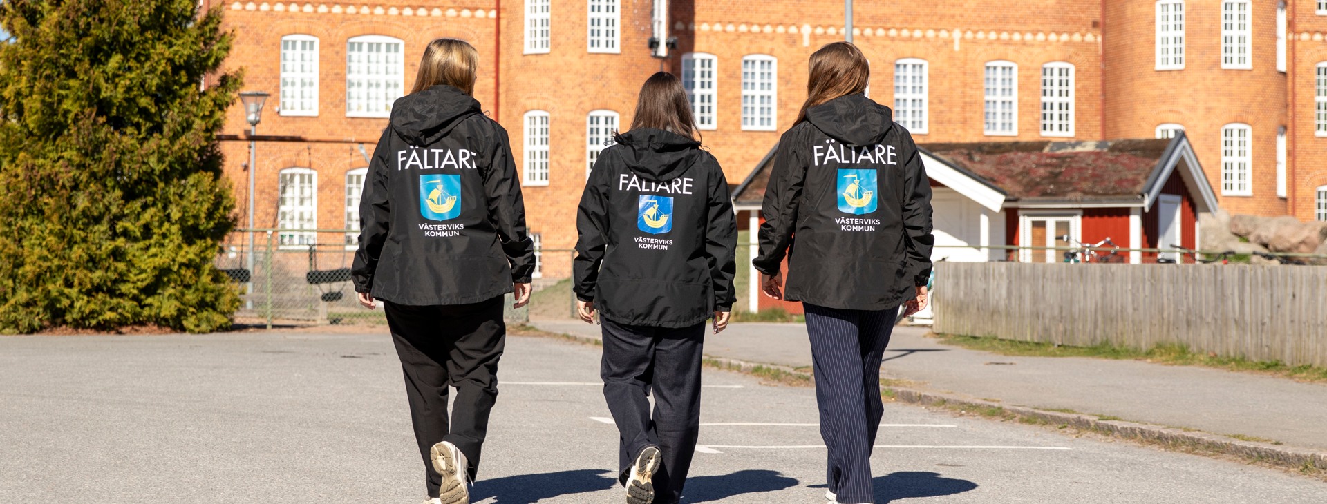 Ryggen på tre fältare utanför Marieborgsskolan med texten "fältare" på jackorna.