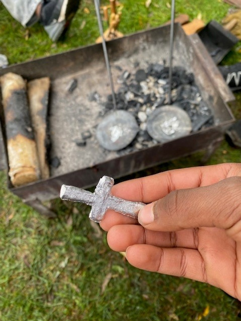 Hand osm håller fram ett kors i tenn som barnen skapat.