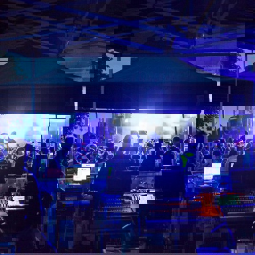 Personer vid mixerbord och publik framför en scen med en artist. 