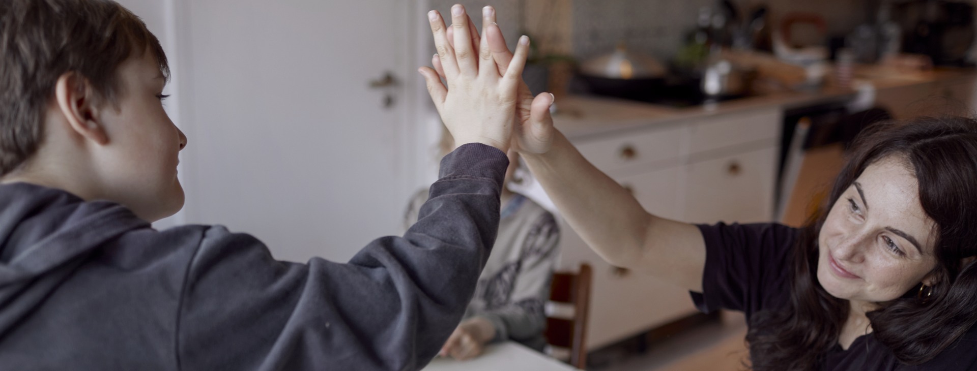Mamma och son gör high five över middagsbordet.