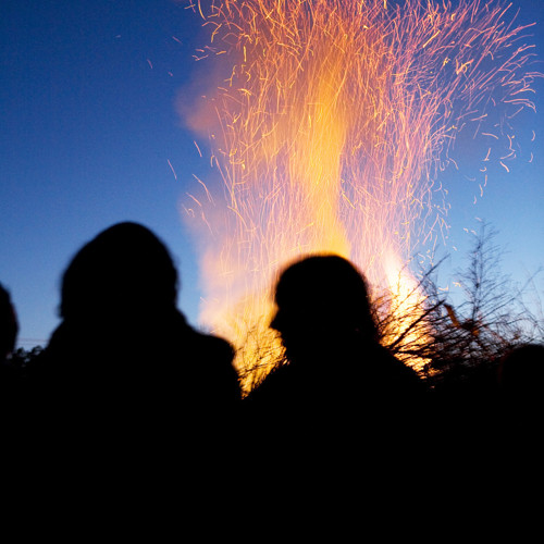 Människor som står framför brinnande valborgsmässoeld. 