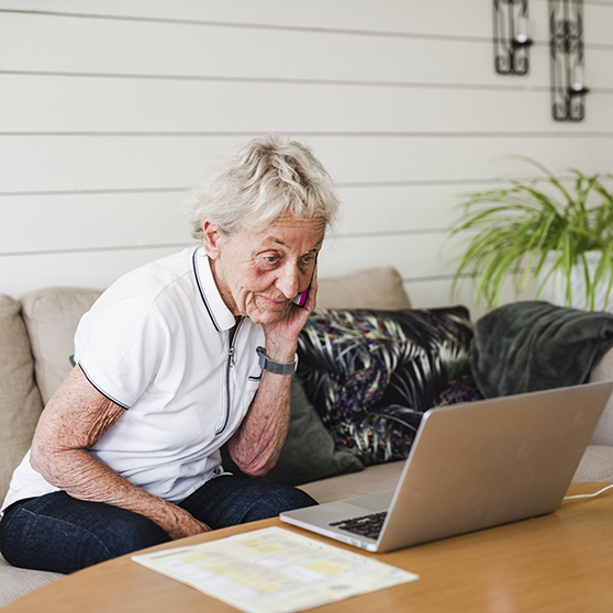 äldre kvinna i soffa med telefon och dator